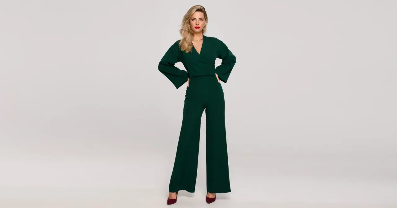 Elegancka kobieta w zielonym kombinezonie z szerokimi nogawkami. Góra kombinezonu ma dekolt kopertowy i szerokie rękawy.