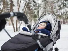 Śpiące dziecko w wózku, ciepło ubrane, pokazuje, jak ubrać noworodka na zimowy spacer.