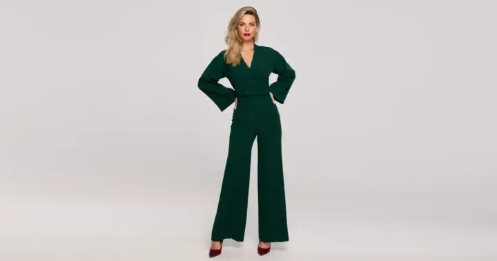 Elegancka kobieta w zielonym kombinezonie z szerokimi nogawkami. Góra kombinezonu ma dekolt kopertowy i szerokie rękawy.